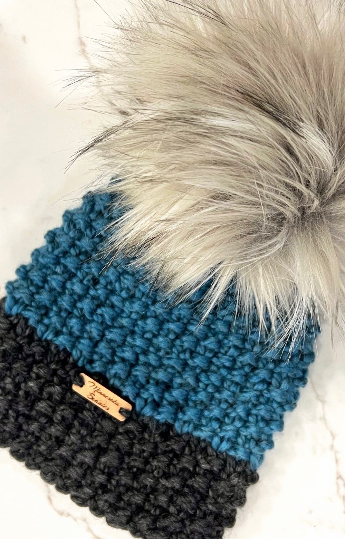 Handmade teal blue and black beanie with oversized white gray faux-fur pom