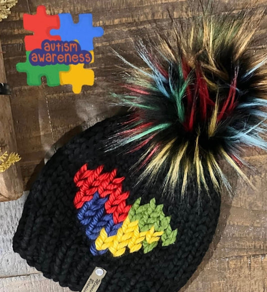 Black handmade beanie with colorful puzzle-inspired design and multicolor faux-fur pom